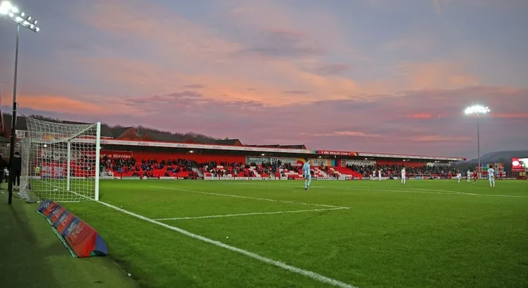 Cảnh sân vận động Crown Ground vào ngày diễn ra trận đấu của Accrington Stanley, với khán giả và cầu thủ trên sân.