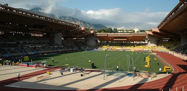 Góc nhìn từ khán đài sân Stade Louis II ra mặt sân cỏ xanh mướt và đường chạy điền kinh, tạo không gian mở