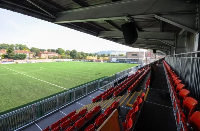 Góc nhìn từ khán đài sân vận động Meadowbank, cho thấy toàn cảnh sân bóng 3G chất lượng FIFA và không gian khán đài đứng đặc trưng.