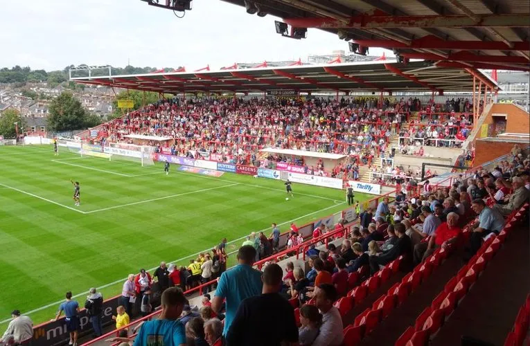 Không khí cuồng nhiệt trên khán đài St. James Park Exeter vào một ngày thi đấu, với các cổ động viên Exeter City hò reo cổ vũ.