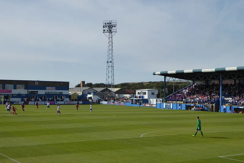 Một trận đấu bóng đá đang diễn ra trên sân cỏ Holker Street, Barrow
